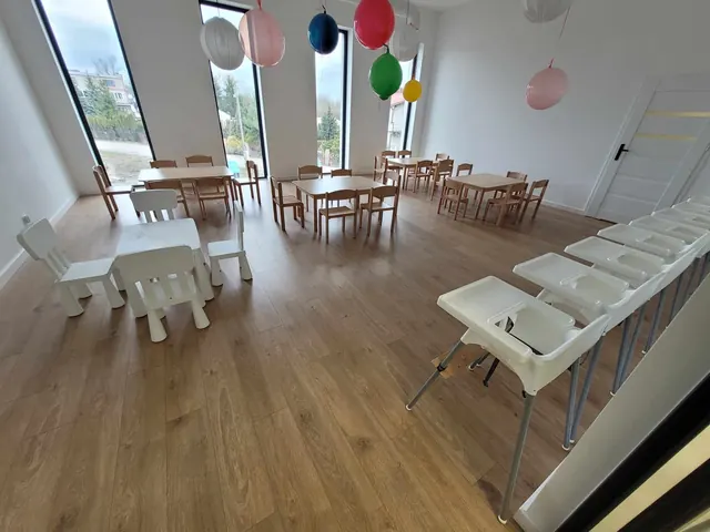 Sala udekorowana balonami, z rzędem białych stolików