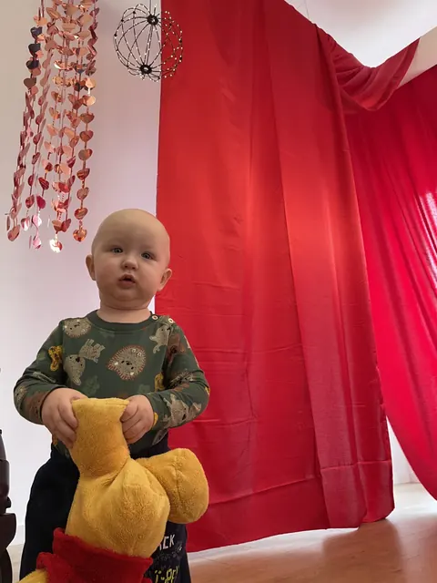 Maluch z pluszowym misiem na tle czerwonej kurtyny